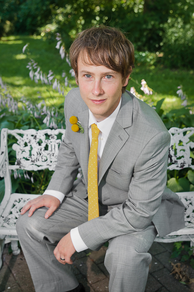 Good looking groom sitting on bench at Whestone Park of Roses