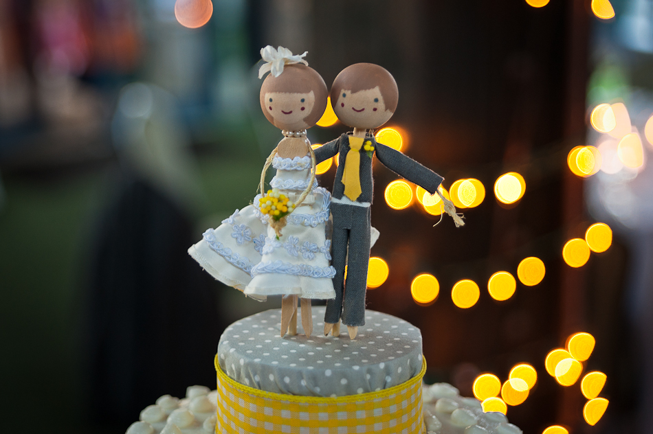 close up of bride and groom cake topper with lights in the background