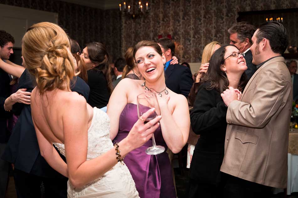 Ecstatic maid of honor with bride at reception with guests dancing