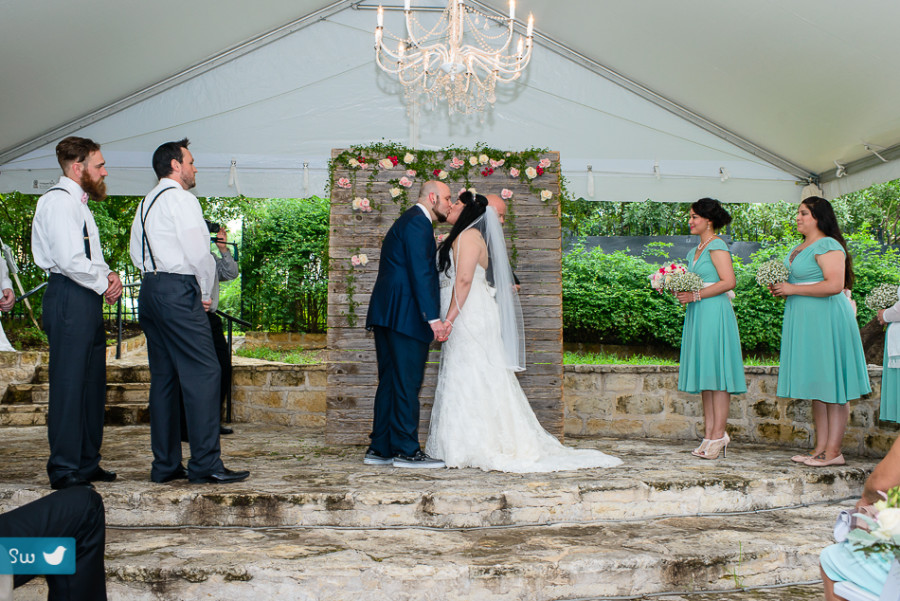 bride and groom kiss in front of flower wall